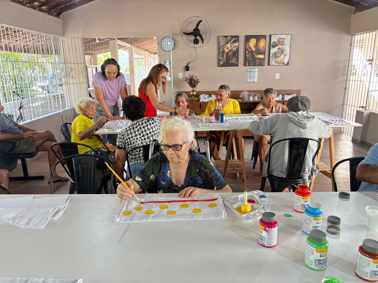 Idosos da AMEM participando de atividade de pintura em ambiente de convivência.